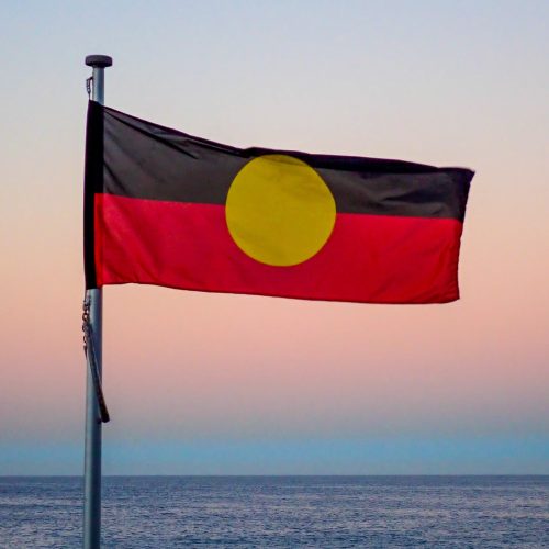 The Australian Aboriginal flag flies at Bondi Beach, Sydney at sunset in winter on 16 June 2023.  In the background is the Pacific Ocean.